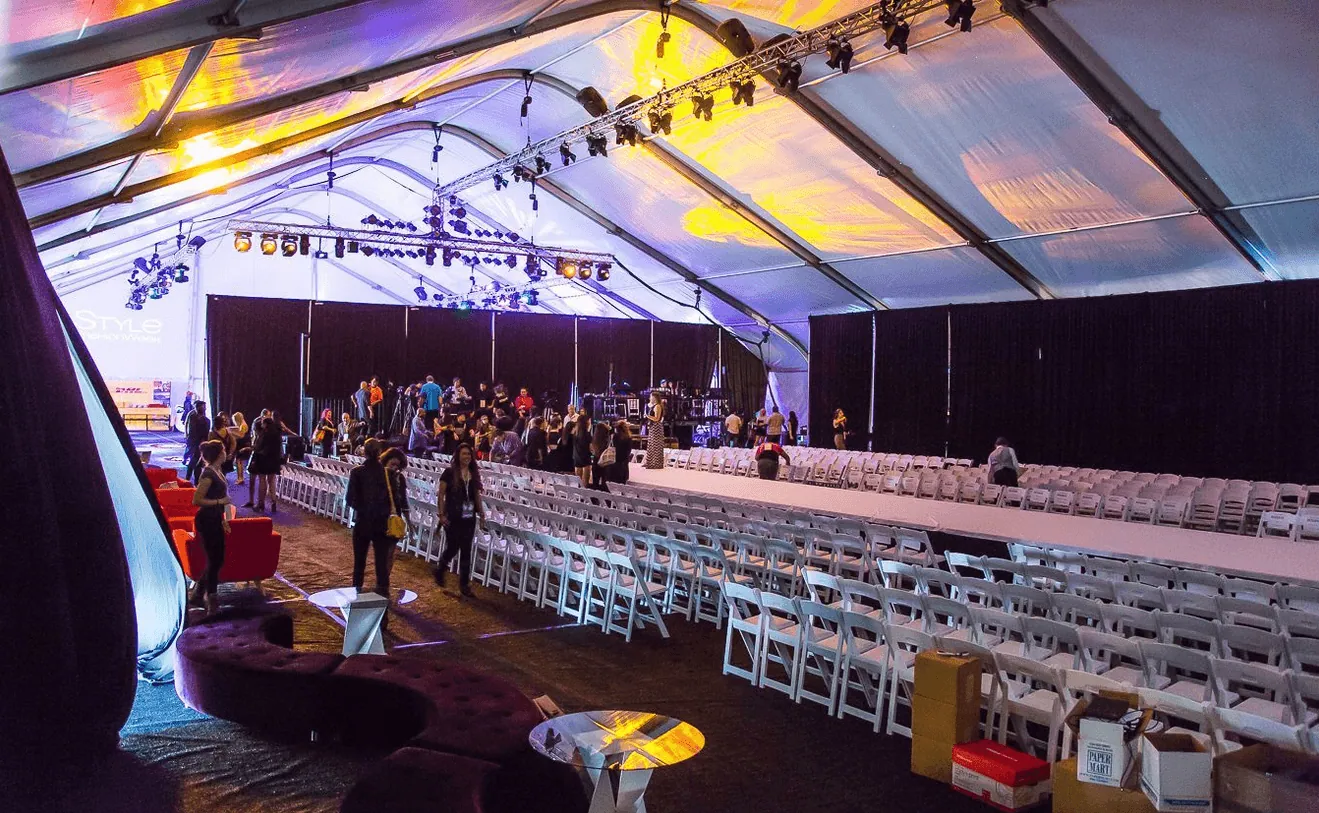 Rows of white chairs set along a runway inside an event tent